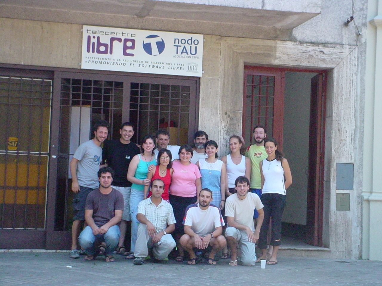 Grupo de personsa posando frente a una casa con ventanas con rejas y una puerta abierta. Un cartel sobre la puerta y ventana informa Telecentro Libre Nodo TAU.