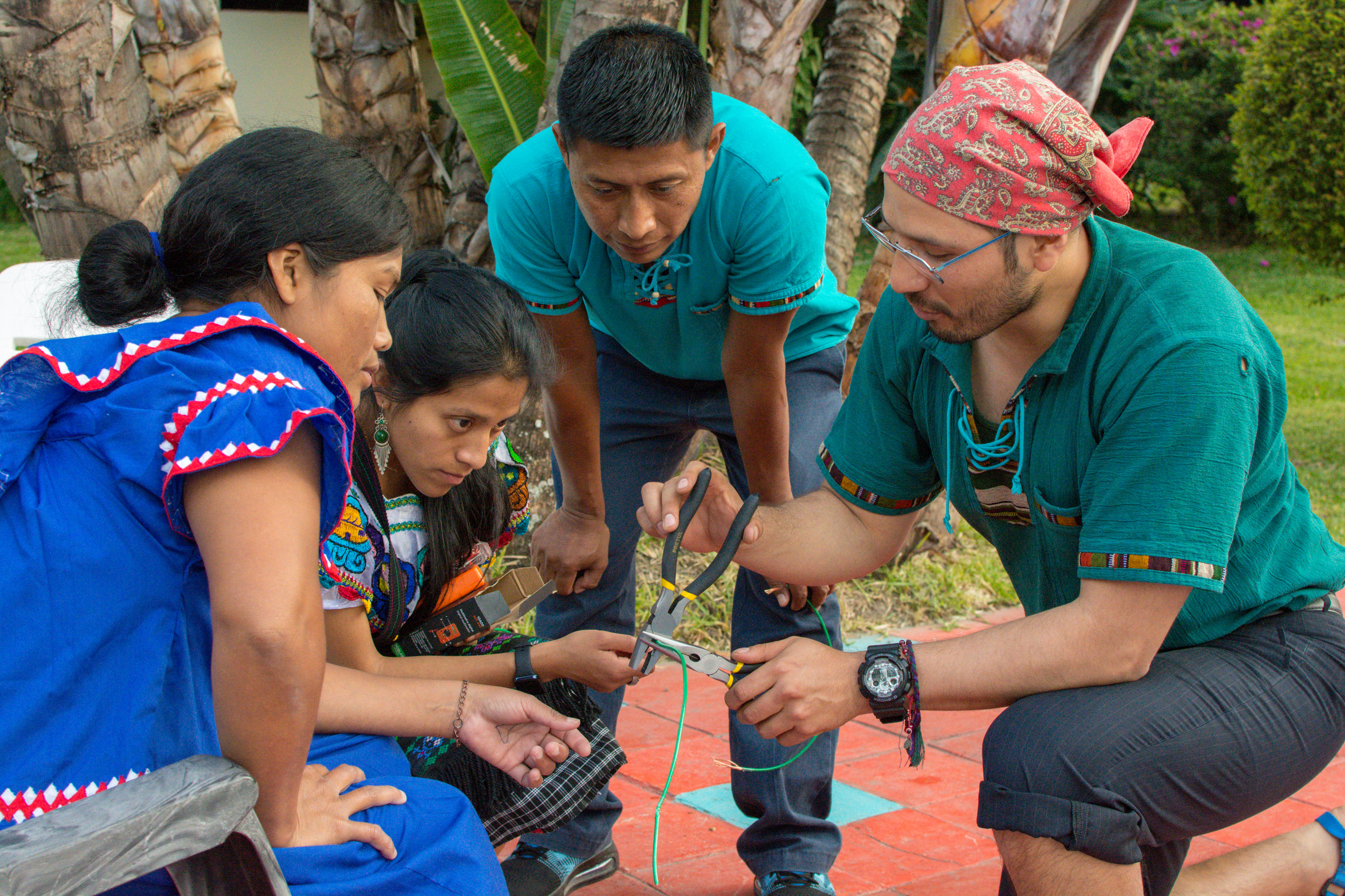 Un grupo de 4 personas, dos varones y dos mujeres, observando el trabajo que uno de e loos realiza con dos pinzas con unos cables.