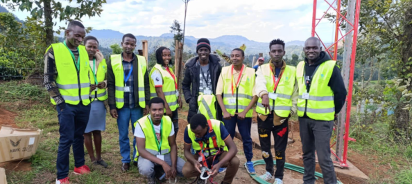 The trainee cohort at the site during the installation of a 21-meter-high guyed wire tower.