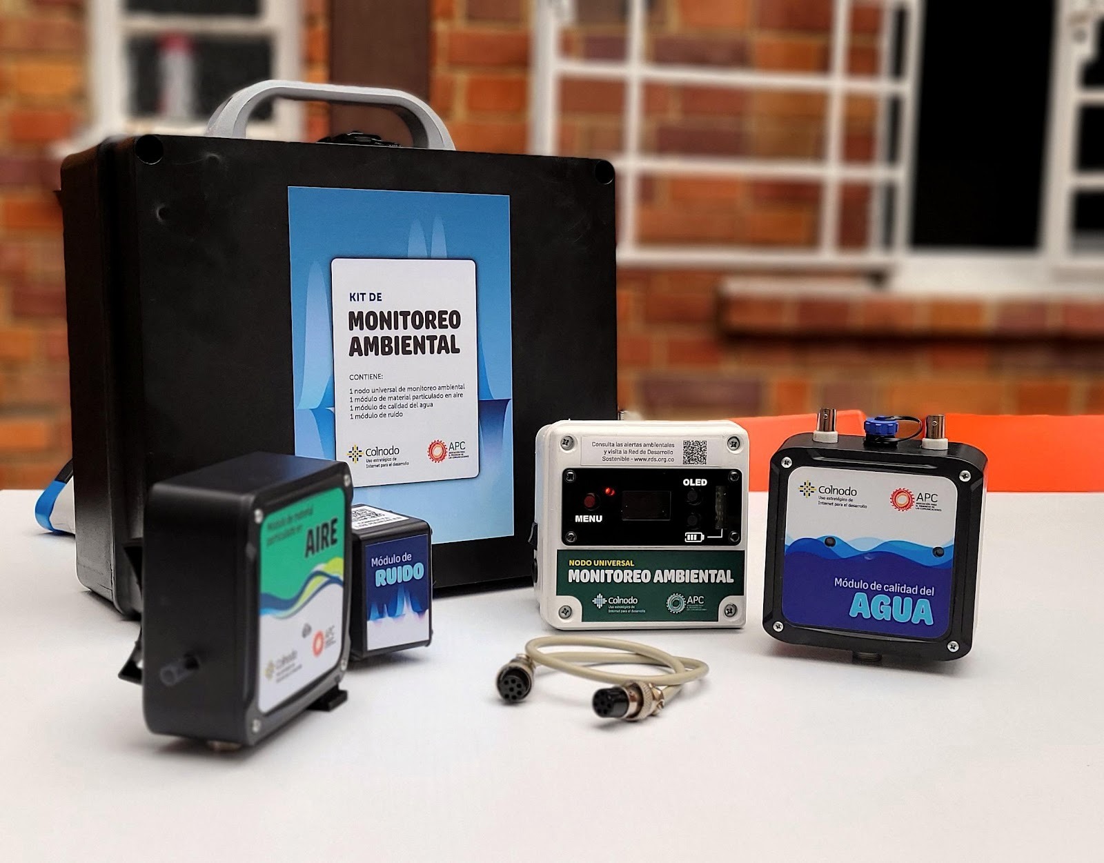 A set of environmental monitoring devices, including air, noise, and water quality modules, with a carrying case and cables, displayed on a table indoors.