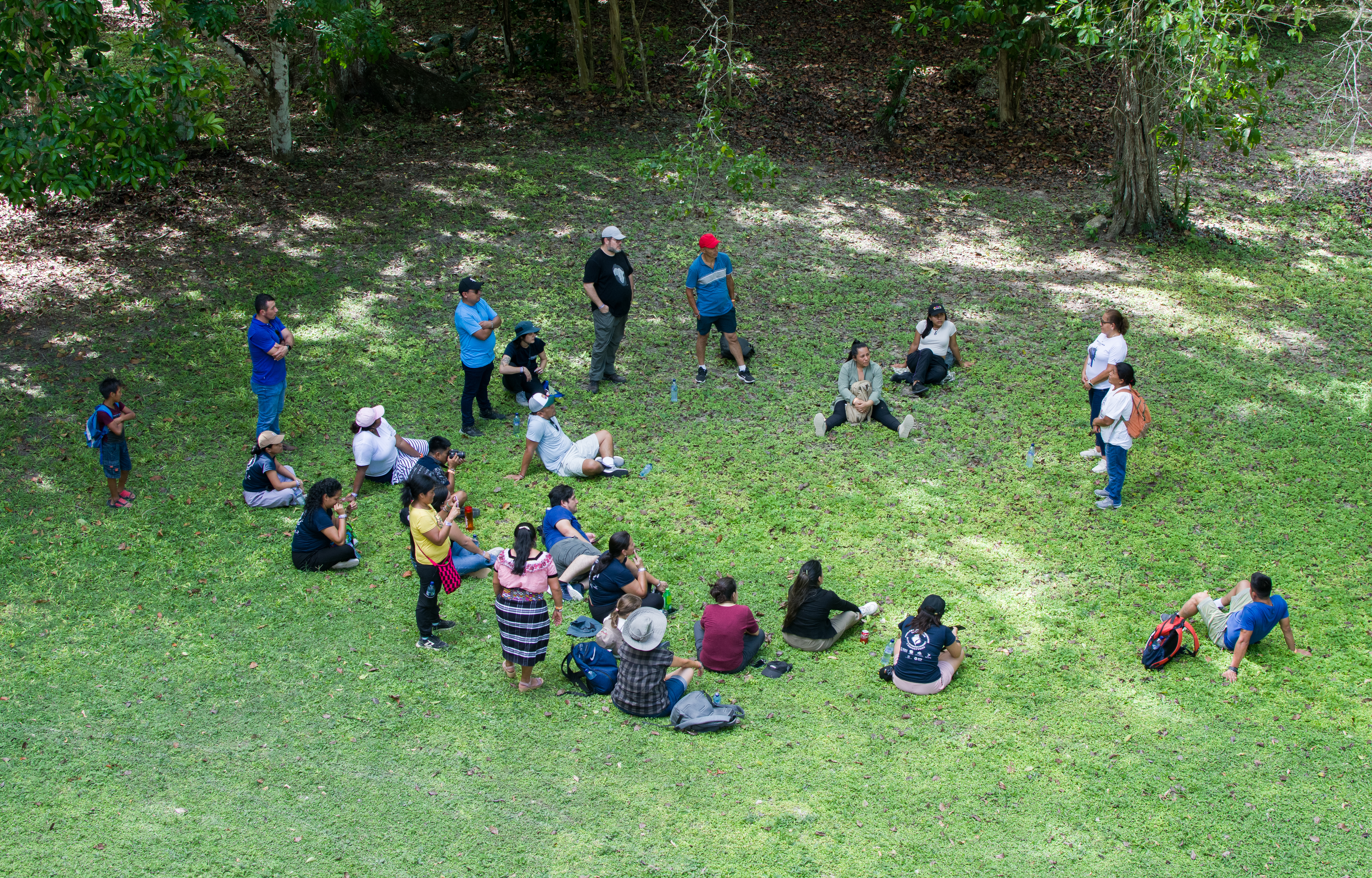 Una rona de personas sentadas sobre el césped tomada la imagen dese la altura.