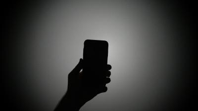Silhouette of a hand holding a mobile phone image linking to Waging war on digital feeds: How platforms and governments fuel violence at the virtual frontline 
